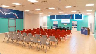 Sala con sedie, tavolo e schermi digitali per dimostrazioni.