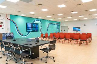 Pareti con grandi schermi digitali, sala con un grande tavolo per conferenze e sedie per il pubblico